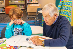older man helping kid read in a school setting