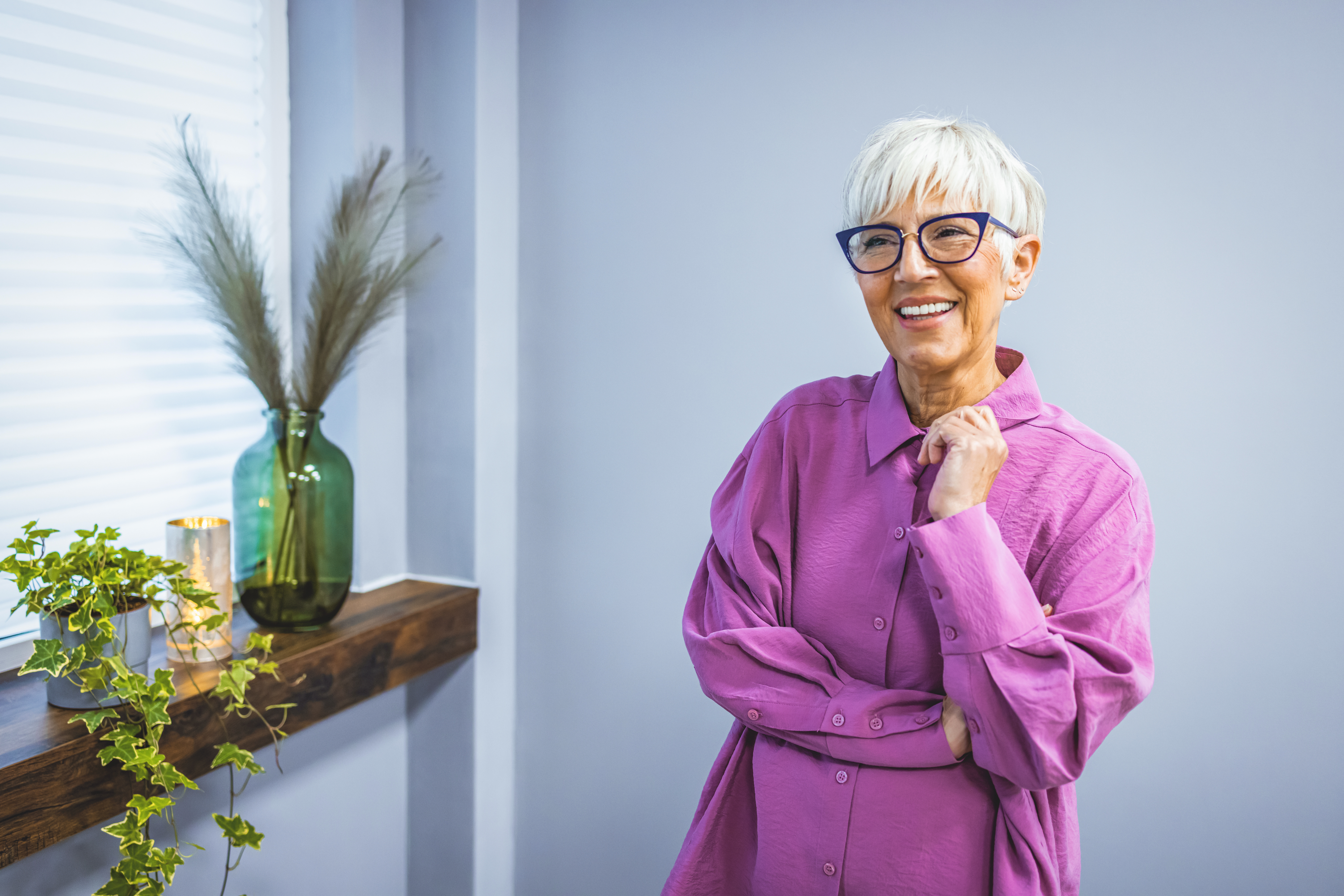 Portrait of mature woman with eyeglasses on grey background. Portrait of cheerful mature woman standing against grey wall. Happy mid woman looking at camera against grey background with copy space